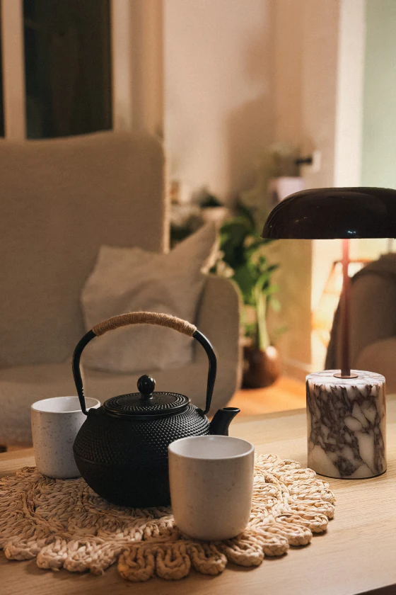 Czarny żeliwny czajnik i dwa kubki na stoliku obok lampki